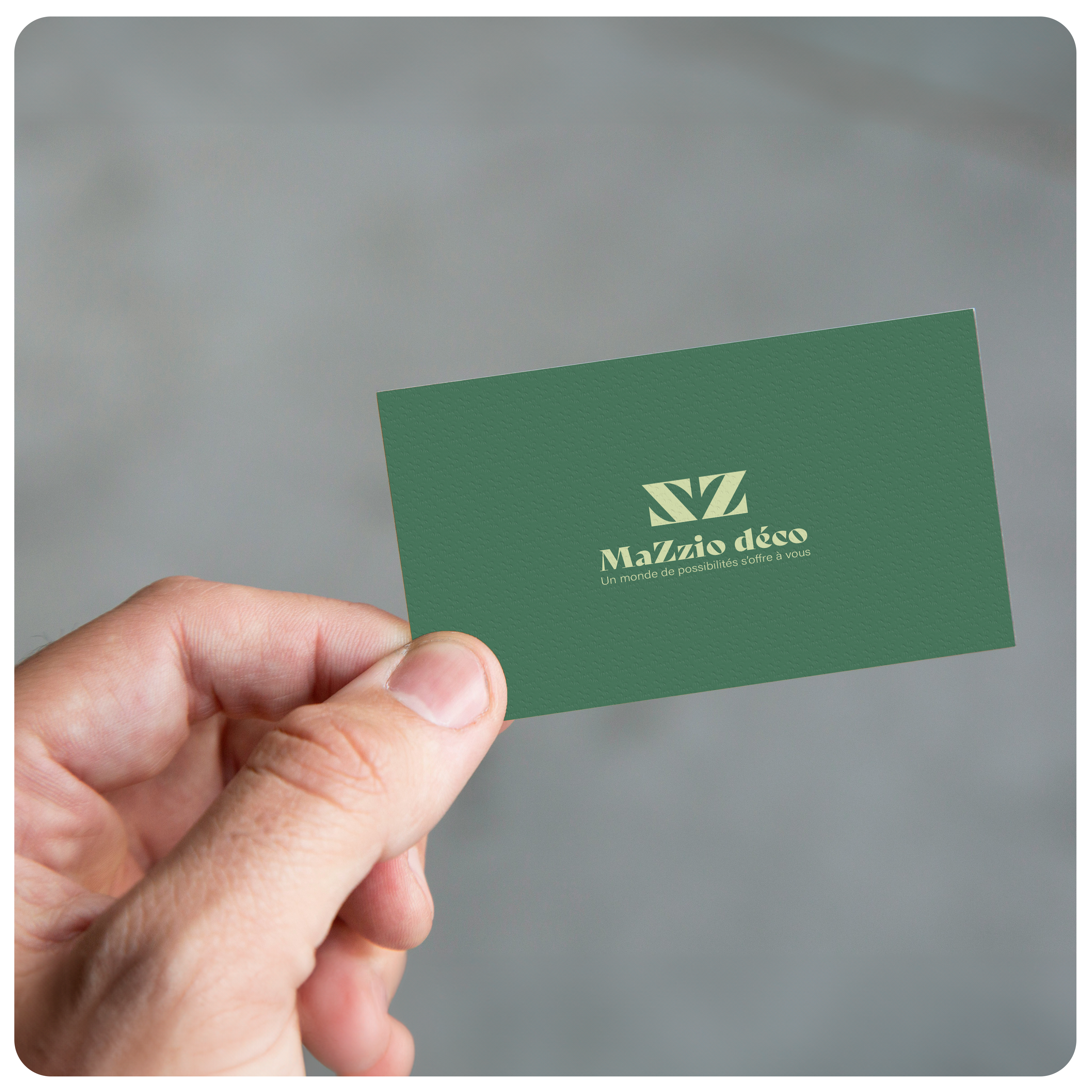 Une main d'homme qui tient entre le pouce et l'index une carte de visite verte MaZzio déco imprimée sur du carton finition semi-mat.